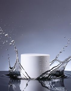 a white cup with water splashing out of it's sides on a reflective surface