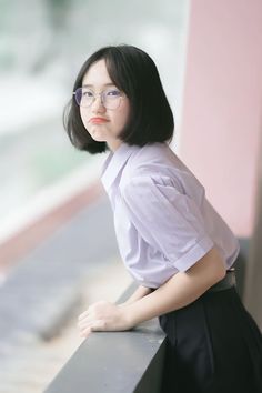 a young woman wearing glasses leaning on a wall with her hand on her hips and looking off to the side