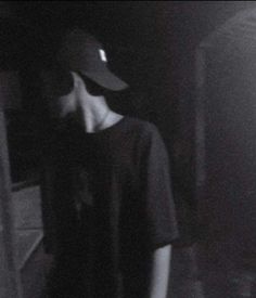 a person standing in the dark with a hat on and wearing a t - shirt