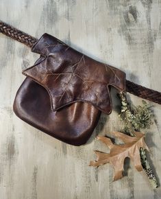 a brown leather pouch sitting on top of a wooden table next to an oak leaf