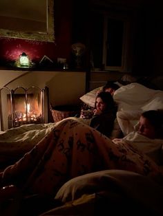 two people are laying in bed next to a fire place