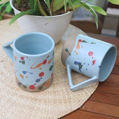 two coffee mugs sitting on top of a table next to a potted plant