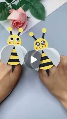 someone is holding two paper bees in front of a pink rose and one has it's face cut out to look like a bee