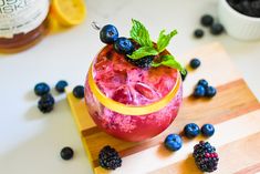 a drink with blueberries, raspberries and lemons on a cutting board