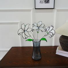 a vase filled with white flowers sitting on top of a wooden table next to a lamp