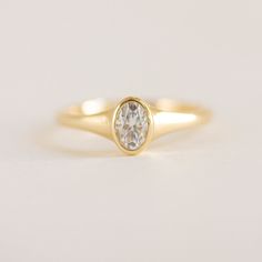 a yellow gold ring with a white diamond in the center on a plain surface,