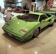 a green sports car is on display in a showroom with other cars behind it