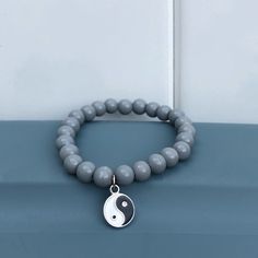 a gray bracelet with a white and black yin sign charm on it's end