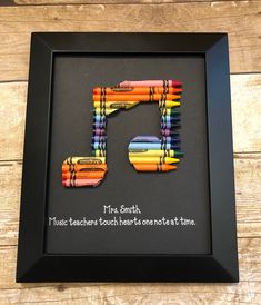 the letter r made out of crayons is in a black frame on a wooden table