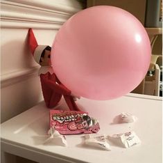 a pink balloon sitting on top of a table next to a candy bar and a elf