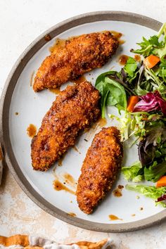 two pieces of fried chicken on a plate next to a salad and breaded crusts