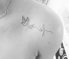 the back of a woman's shoulder with a small bird flying above her shoulder