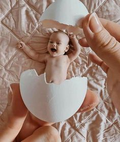 a baby in an egg shell being held by someone's hands over a bed