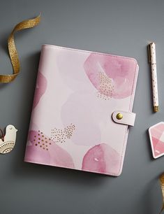 a pink flowered notebook with gold trimmings next to a pen and other items