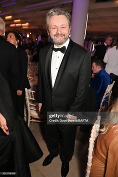 a man in a tuxedo and bow tie standing next to other people at an event