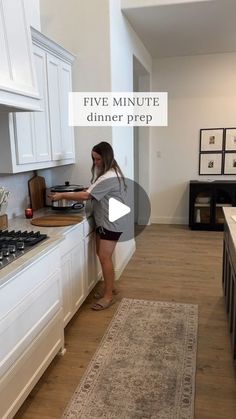 a woman standing in front of a stove top oven next to a kitchen counter with white cabinets