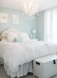 a white bed sitting in a bedroom under a chandelier next to a window