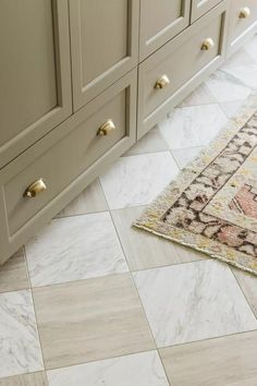 a bathroom with marble flooring and beige cabinetry, including a rug on the floor