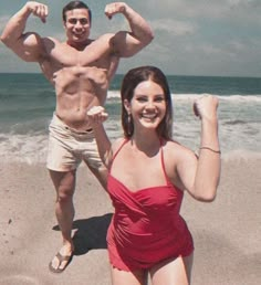 a man and woman posing on the beach with their arms in the air as they pose for a photo