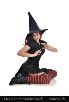 a woman dressed as a witch sitting on the floor with her legs crossed and wearing striped stockings