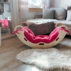 a child's rocking chair with pink cushions on the floor in front of a couch