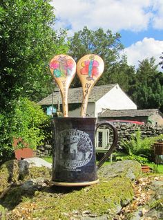 two wooden spoons sticking out of a coffee cup on top of moss covered rocks