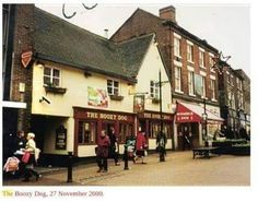 an old photo of people walking in front of shops on a city street with buildings