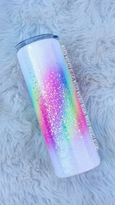 a rainbow colored glitter tumbler sitting on top of a white fur covered floor next to a brush