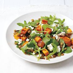 a white plate topped with spinach and sweet potato salad on top of a table