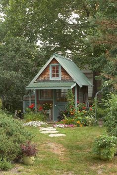 a small wooden house in the middle of some trees and flowers, with a pathway leading to it