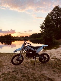 a dirt bike parked next to a body of water at sunset or dawn with clouds in the sky