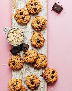 chocolate chip cookies and oatmeal are arranged on a wooden board next to a spoon