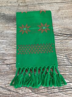 a green scarf with red dots and tassels on a wooden surface, resting on a piece of wood