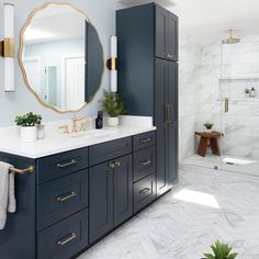 a bathroom with blue cabinets and white marble counter tops, gold accents on the mirror