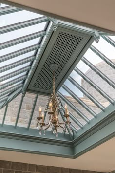 a chandelier hanging from the ceiling in a room with glass walls and skylights