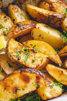 cooked potatoes with parsley and lemon in a white dish on top of a wooden table