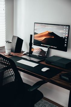 a desktop computer sitting on top of a wooden desk next to a black chair and window