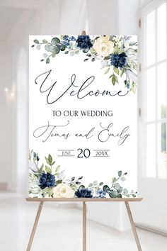 a welcome sign with flowers and greenery is displayed in front of a white wall