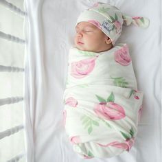 a baby wrapped in a blanket sleeping on top of a white sheet with pink flowers