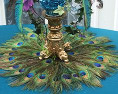 a vase with flowers and peacock feathers on a blue table cloth in front of a window