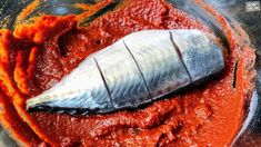 a fish in a bowl with red sauce on the side and an orange substance next to it