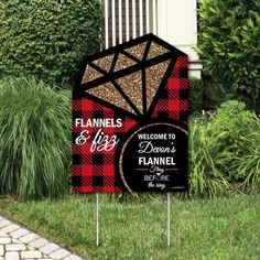 a black and red sign sitting on top of a lush green field next to bushes