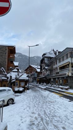 a snowy street with cars parked on the side and buildings in the backgroud