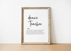 a framed poster with the words dance teacher written in black on it next to a wooden table