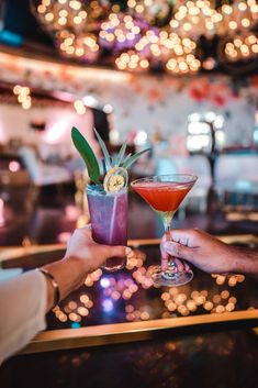 two people holding up cocktails on a table