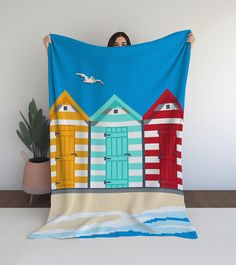 a woman holding up a quilt with beach huts on it