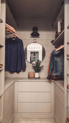 a walk in closet with clothes hanging on the shelves and a round mirror above it