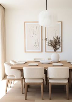 a dining room table with white chairs and pictures on the wall