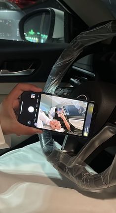 a person holding a cell phone in their hand and recording something on the car dashboard