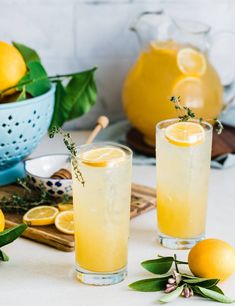 two glasses filled with lemonade sitting on top of a table next to sliced lemons